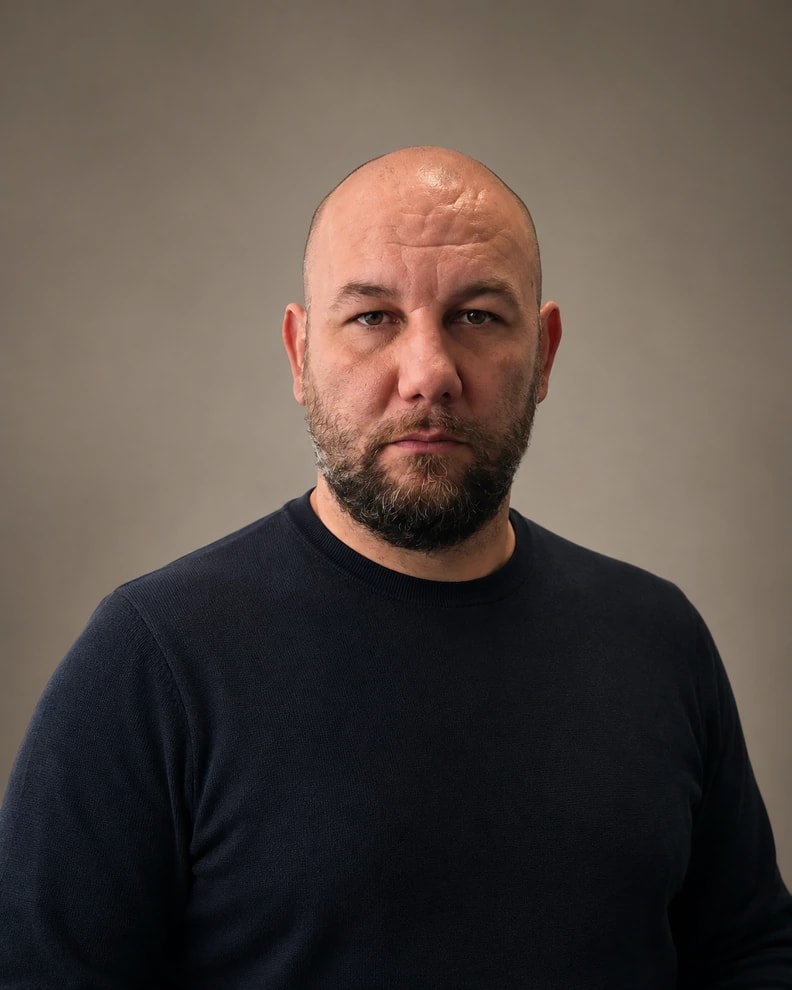 Omar Beglerović, photographed head and shoulders against a plain warm-grey backdrop, looking straight into the camera.